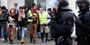 Eine Gruppe von menschen, im Vordergrund zwei Polizisten mit helmen und Schlagstöcken