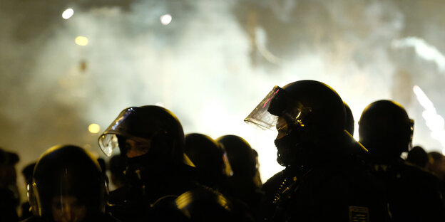 Behelmte Polizisten im Gegenlicht vor Rauchschwaden
