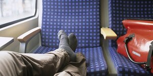 In der Bahn: Eine Mann legt sein Füsse hoch, außerdem ist eine Fahrradtasche auf dem Sitz abgelegt