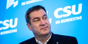 Markus Söder sitzt vor einem Plakat mit dem Schriftzug der CSU und schaut zur Seite