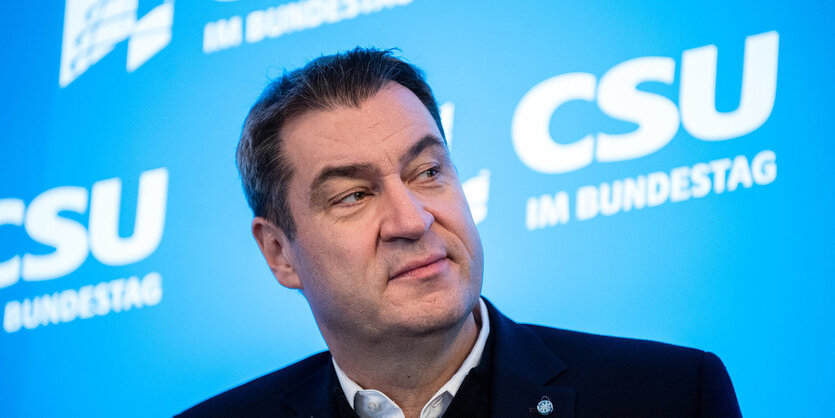 Markus Söder sitzt vor einem Plakat mit dem Schriftzug der CSU und schaut zur Seite