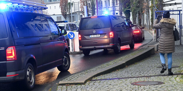 Zwei schwarze Vans fahren auf einer Straße, auf dem Bürgersteig daneben eine Frau