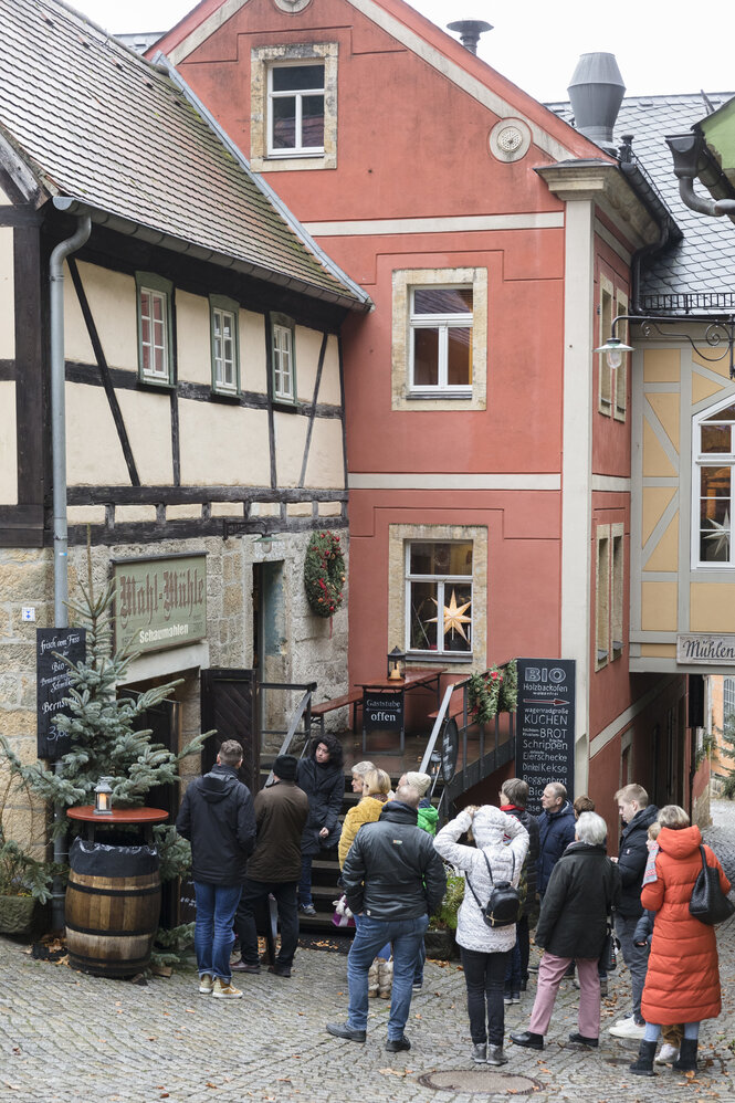 Menschen gehen eine Straße entlang, links ist die alte Mühle in einem Fachwerkhaus