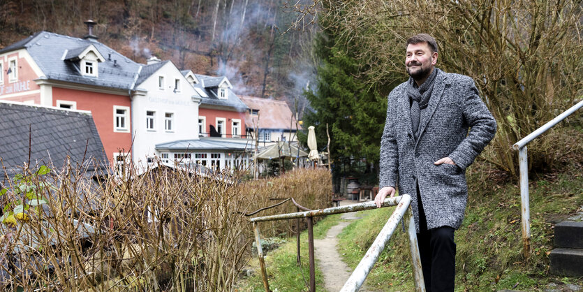 Ein Mann steht an einem Zaun, im Hintergrund sind Häuser zu sehen