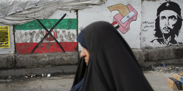 Eine Frau geht in Bagdad an einer Mauer mit einer durchgestrichenen iranischen Flagge vorbei.