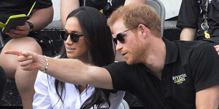 Prinz Harry deutet mit dem Finger auf etwas außerhalb des Bildes, Maghan guckt hin