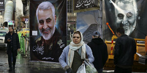 Straßenszene,eine Frau mit Einkaufstaschen, im Hintergrund zwei Poster mit dem Gesicht von Qasim Soleimani