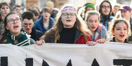 Demonstrantinnen tragen ein Banner, eine Frau trägt ein Stirnband mit der Aufschrift "Stop Adani"