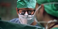 Zwei Chirurgen tragen OP Hauben und eine Lupenbrille, sie unterhalten sich
