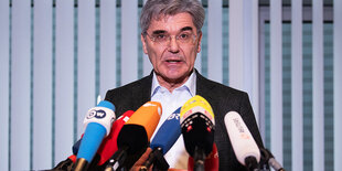 Joe Kaeser steht hinter einer Reihe von Mikrofonen