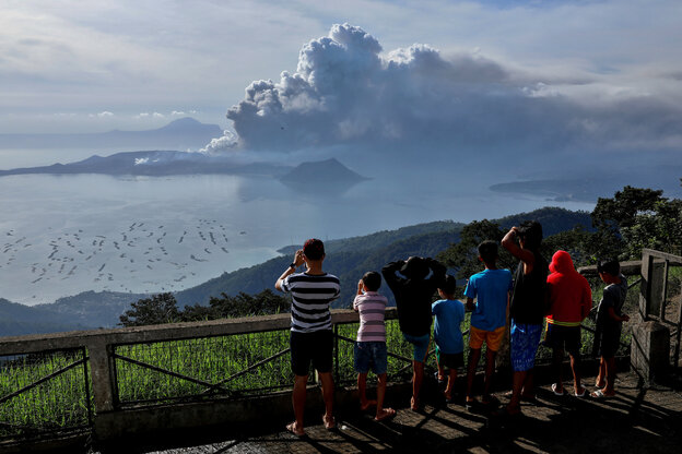 Menschen auf einem grünen Hügel gucken auf einen in der Ferne dunkle Wolken spuckenden Vulkan