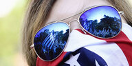Eine Frau mit Sonnenbrille hat sich eine USA-Flagge vor die untere Gesichtshälfte gebunden