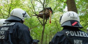 Zwei Polizisten von hinten, vor einem Baumhaus im Hambacher Wald stehend