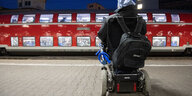 Mann im Rollstuhl steht auf dem Bahnsteig und blickt auf einen roten Zug