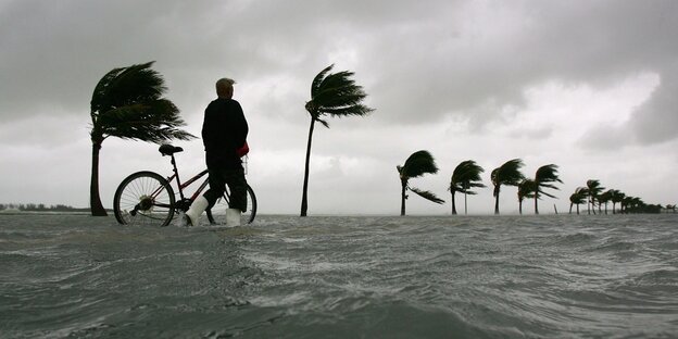 Ein Mann steht mit seinem Fahrrad auf einer überfluteten Küstenpromenade