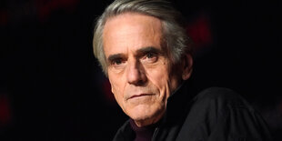 Der Schauspieler Jeremy Irons ist vor schwarzem Grund zu sehen und schaut ernst.