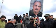 ein Mann in einer Menschenmenge trägt ein Plakat mit dem Foto des Generals Haftar