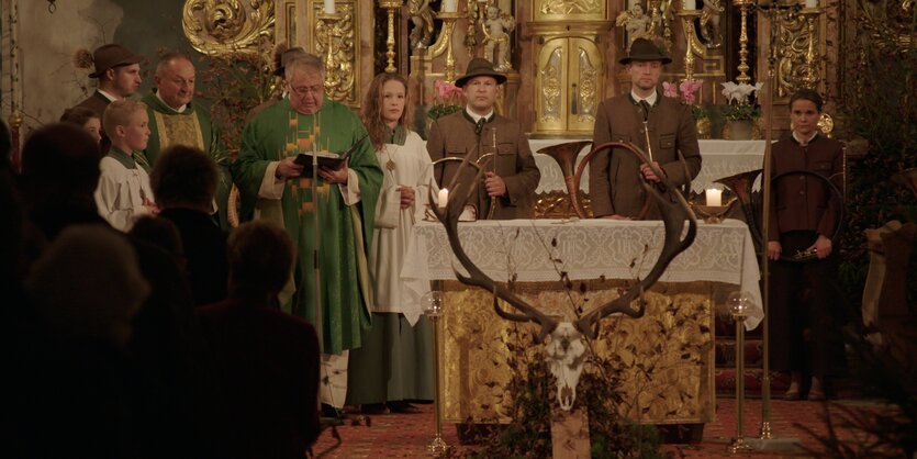 Mehrere Menschen in Jagduniformen vor einem Altar