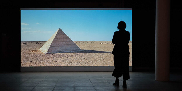 Person steht vor einem hell beleuchteten Bild einer Pyramide