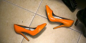 Orangefarbener Stöckelschuhe liegen auf einem Fliesenboden