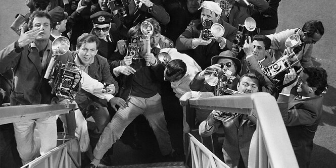 Ein Still aus dem Fill La Dolce Vita zeigt eine hysterische Gruppe von Fotografen, die unterhalb einer Treppe nach oben schauen