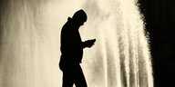 Mann steht mit dem Smartphone vor einem Brunnen