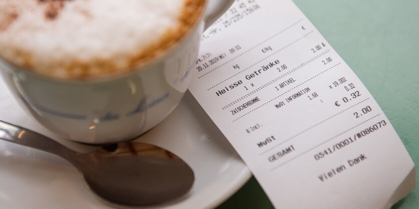 In einem Café liegt neben einer Tasse Cappuccino eine Quittung für diesen.