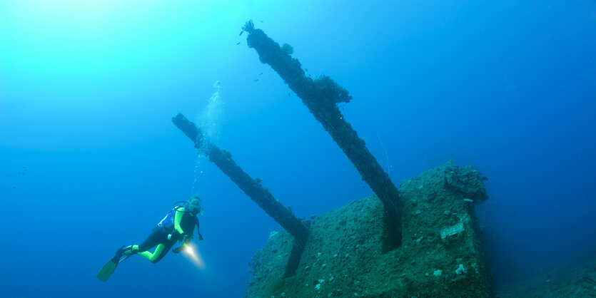 Ein Taucher schwimmt um das Doppelgeschütz eines untergegangenen Militärschiffes