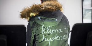 Projektion des Wortes Klimahysterie auf einen grünen Mantel mit Pelzkapuze