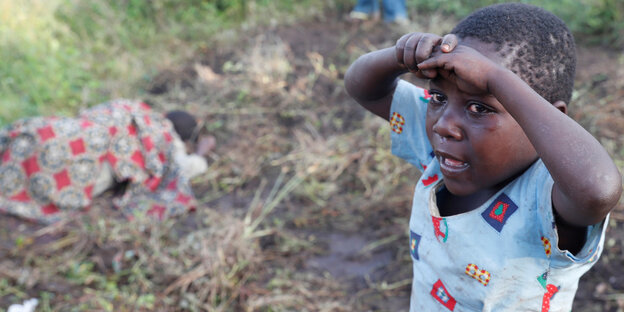 Ein Kind weint, umscharf liegen im Hintergrund Körper auf der Erde