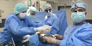 vier Ärzte im OP-Raum mit blauen Kitteln und Mundschutz