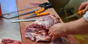 Ein Arbeiter zerteilt mit einem langen Messer rohes Fleisch.
