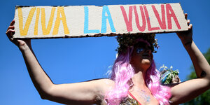 Eine weibliche Person hält auf dem CSD in Freiburg 2018 ein Schild in die Luft, auf dem "Viva la Vulva" steht. Die Persoin hat lange pinke Haare. Im Gesicht trägt sie Glitzer