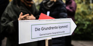 Schild mit der Aufschrift "Die Grundrente kommt" vor einer Gesprächsrunde mit Bundesarbeitsminister Hubertus Heil