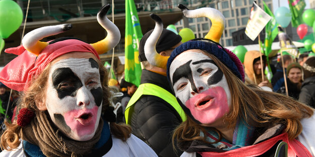 Das Foto zeigt die Gesichter von zwei jungen Frauen, die sich schwarz-weiß wir Kühe angemalt haben und Hörner auf dem Kopf tragen. Sie sind Teilnehmerinnen der Wir-haben-es-Satt-Demo im Jahr 2018.