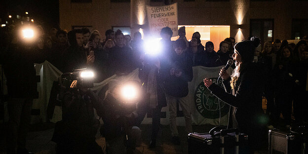 Luisa Neubauer steht in der Dunkelheit und spricht in ein Mikrofon, darum andere AktivistInnen