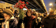 Trauernde Menschen, im Zentrum Frau mit Kopftucj, Kerze und Blumen in der Hand
