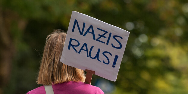 Eine Frau von hinten, die ein Schild "Nazis raus" trägt