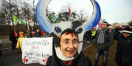 Eine Frau trägt eine Rindmaske, im Hintergrund halten Demonstrierende einen Banner.