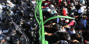 Migranten gehen auf eine Polizeikette an einem Grenzzaun los