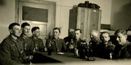schwarz-weiß-Foto. Mehrere Uniformierte sitzen mit Bier an einem Tisch