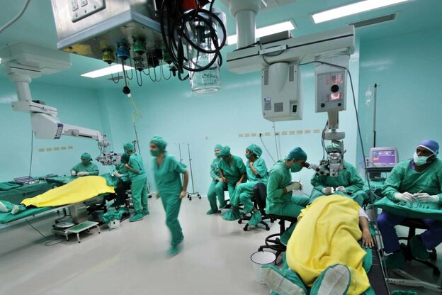 Ärzte in grünen OP Kitteln und Mundschutz, 2 Patienten auf der Bahre, technische Geräte über dem GEsicht