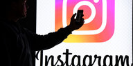 Ein Mann hält ein Smartphone vor einem Monitor mit dem Logo von Instagram