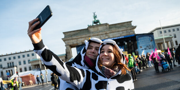 Zwei Demonstranten, die als Kühe verkleidet sind, machen vor dem Brandenburger Tor ein Selfie.