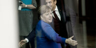 Angela Merkel und Emmanuel Macron strecken die Hand aus, aber in verschiedene Richtungen