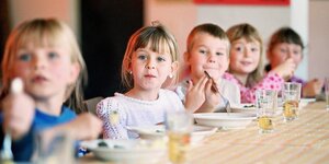 Kinder sitzen vor Tellern und Getränken