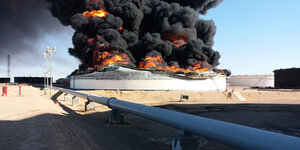 Ein brennender Öltank in Libyen mit einer Pipeline im Vordergrund.