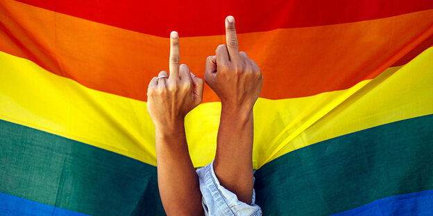 Zwei ausgestreckte Mittelfinger vor einer Regenbogenflagge.