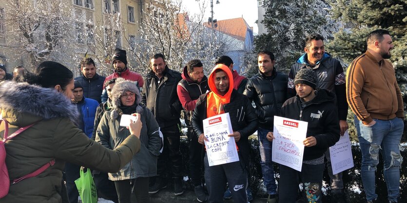 Menschen demonstrieren mit Plakaten und werden von einer Frau mit Handy fotografiert