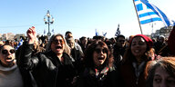 Demonstrantinnen rufen Slogans und tragen eine Griechische Fahne.